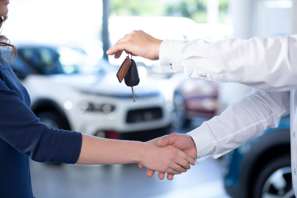 Two people shaking hands and passing car keys and after selling a used car